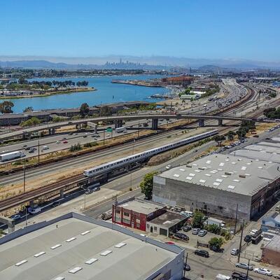 A BART train rides the rails in Oakland, with San Francisco's skyline visible in the distance across the water