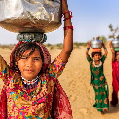 A young woman in India carries well water on her head while two friends trail behind