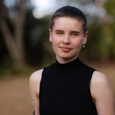 woman with short hair stands infront of trees