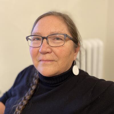 woman with braid, black turtleneck, and glasses looks at camera 