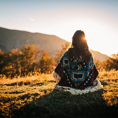 An Indigenous woman sits in nature with her back to the camera