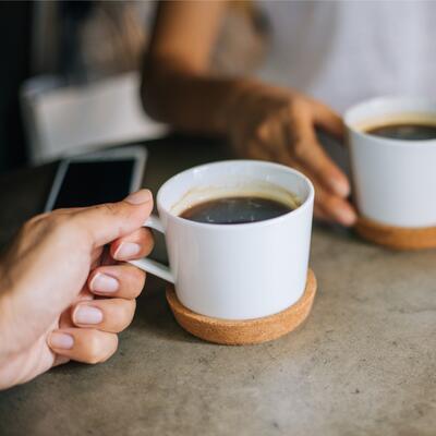 Two people hold coffee cups in their hands while seated at a table