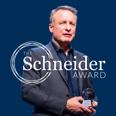 Jonathan Foley holding Schneider Award with Schneider Award logo in front of him