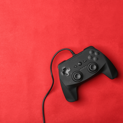 Basic black video game controller with a cord running out of the frame, set against a red fabric background