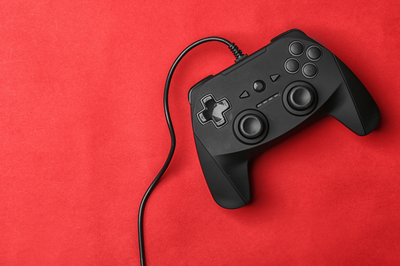 Basic black video game controller with a cord running out of the frame, set against a red fabric background